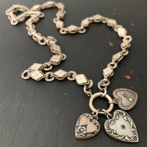 This Victorian-era chain is made of solid sterling silver and features intricately engraved horizontal diamond shapes interspersed with flat circular rings. Paired with a silver or silver and gold locket, this chain instantly makes a necklace more bold and eye-catching.  Shown with sterling silver heart charms