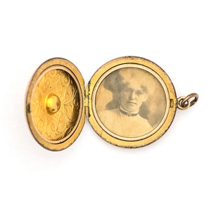 This romantic round Edwardian locket features a playful swirling pattern framing a sizable white paste stone at its center, and a polished verso. It opens to hold two photos, includes both original frames and pairs perfectly with one of our antique gold fill chains. Open locket view