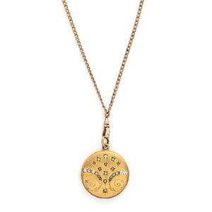 This matte round locket features 23 white glass stones scattered throughout a whimsical pattern of starbursts and ornamental swirls. It opens to hold one photo, includes the original frame and pairs perfectly with one of our antique gold fill chains. Front locket view, shown on chain