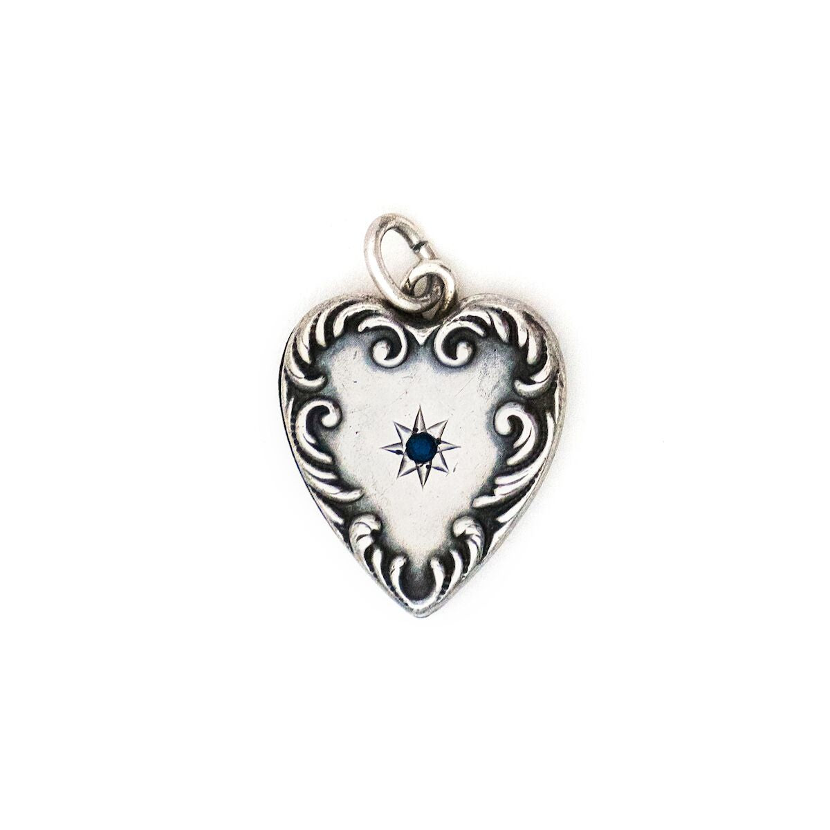 This heart charm is made of sterling silver and features a single blue cabochon stone inlaid in a star setting, and surrounded by a raised and textured border. The initials "AK" are finely etched on the back. Paired with one of our antique silver chains, this heart pendant can be worn both as a pendant or in a cluster of charms. Front charm view