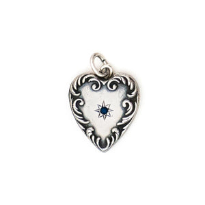This heart charm is made of sterling silver and features a single blue cabochon stone inlaid in a star setting, and surrounded by a raised and textured border. The initials "AK" are finely etched on the back. Paired with one of our antique silver chains, this heart pendant can be worn both as a pendant or in a cluster of charms. Front charm view