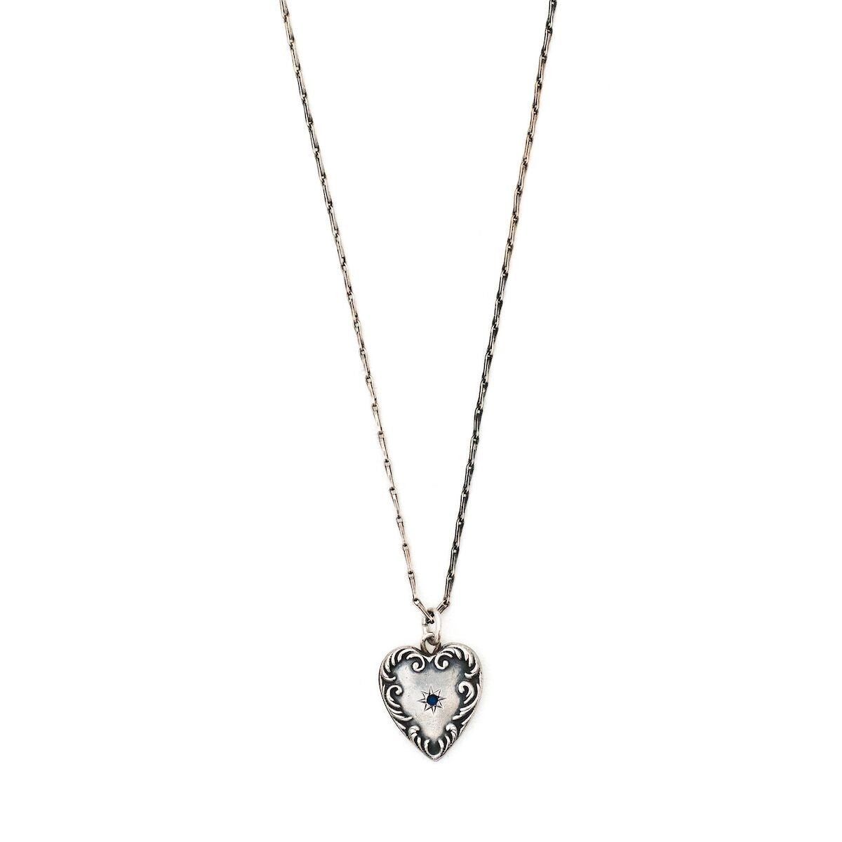 This heart charm is made of sterling silver and features a single blue cabochon stone inlaid in a star setting, and surrounded by a raised and textured border. The initials "AK" are finely etched on the back. Paired with one of our antique silver chains, this heart pendant can be worn both as a pendant or in a cluster of charms. Front charm view