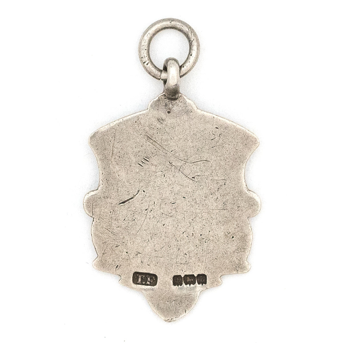 This shield charm is made of English sterling silver and features a rosy shield  surrounded by a smooth ribbon border.  Made in Birmingham, England in 1934, this piece bears the hallmarks for its date (L), silver material (lion), and location (anchor). Paired with one of our antique silver chains, this charm can be worn both as a pendant or in a cluster of charms.  Back charm view, showing english hallmarks