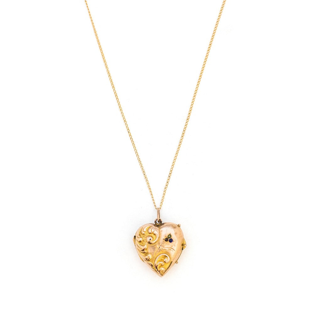 This puffed three dimensional 10K gold heart locket features a swirling raised relief curlicue pattern with a pearl, ruby and sapphire accent. It opens to hold two photos, includes both original frames and pairs perfectly with one of our antique 14K gold chains.  Front Locket View