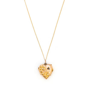 This puffed three dimensional 10K gold heart locket features a swirling raised relief curlicue pattern with a pearl, ruby and sapphire accent. It opens to hold two photos, includes both original frames and pairs perfectly with one of our antique 14K gold chains.  Front Locket View, shown on chain