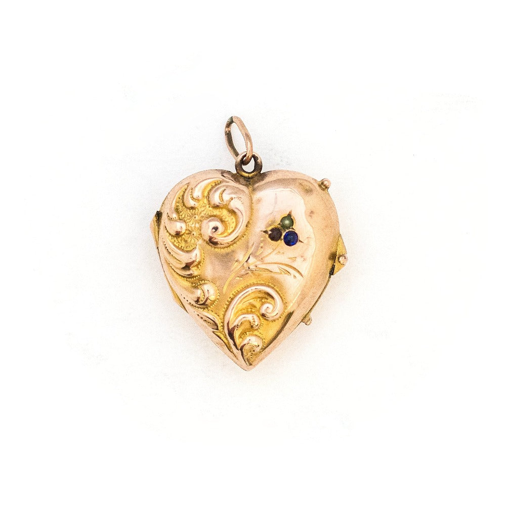 This puffed three dimensional 10K gold heart locket features a swirling raised relief curlicue pattern with a pearl, ruby and sapphire accent. It opens to hold two photos, includes both original frames and pairs perfectly with one of our antique 14K gold chains.  Front Locket View