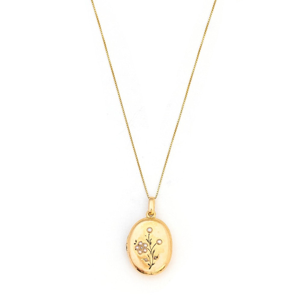 This 18K gold oval locket features 10 pearls scatters throughout a delicate floral design complete with black enamel details. It opens to hold two photos pairs perfectly with one of our antique 14K gold chains. Front Locket View