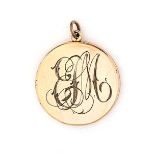 This round locket features a delicately etched wreath of forget-me-not flowers with purple paste stones throughout the design as the flower centers. The initials EM are inscribed on the back. It opens to hold two photos, includes both original frames and pairs perfectly with one of our antique gold fill chains.  Back of locket view