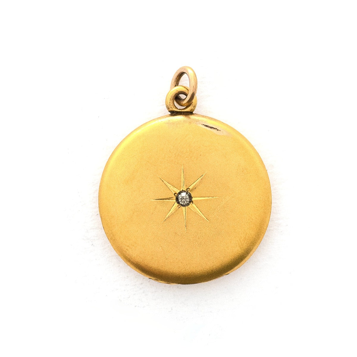 This classic round locket features a simple Victorian starburst with a white paste stone at it's center. It opens to hold two photos, includes one original frame and pairs perfectly with one of our antique gold fill chains. Front locket view