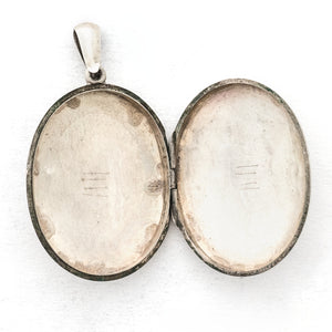 This large sterling silver oval locket features the classic Victorian symbol, a forget-me-not flower surrounded by greenery in a dramatic deep V shape and opens to hold two photos. We have paired this locket with an exquisite engraved Victorian sterling silver book chain from the same era. Open locket view