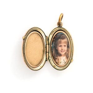 This unique oval locket features a delicate design with sky, navy blue and black enamel set on a finely textured background. The background features floral accents and a cross bar in the same instricate style. It opens to hold two photos, includes both original frames and glass and pairs perfectly with one of our antique gold fill chains.  Open locket view