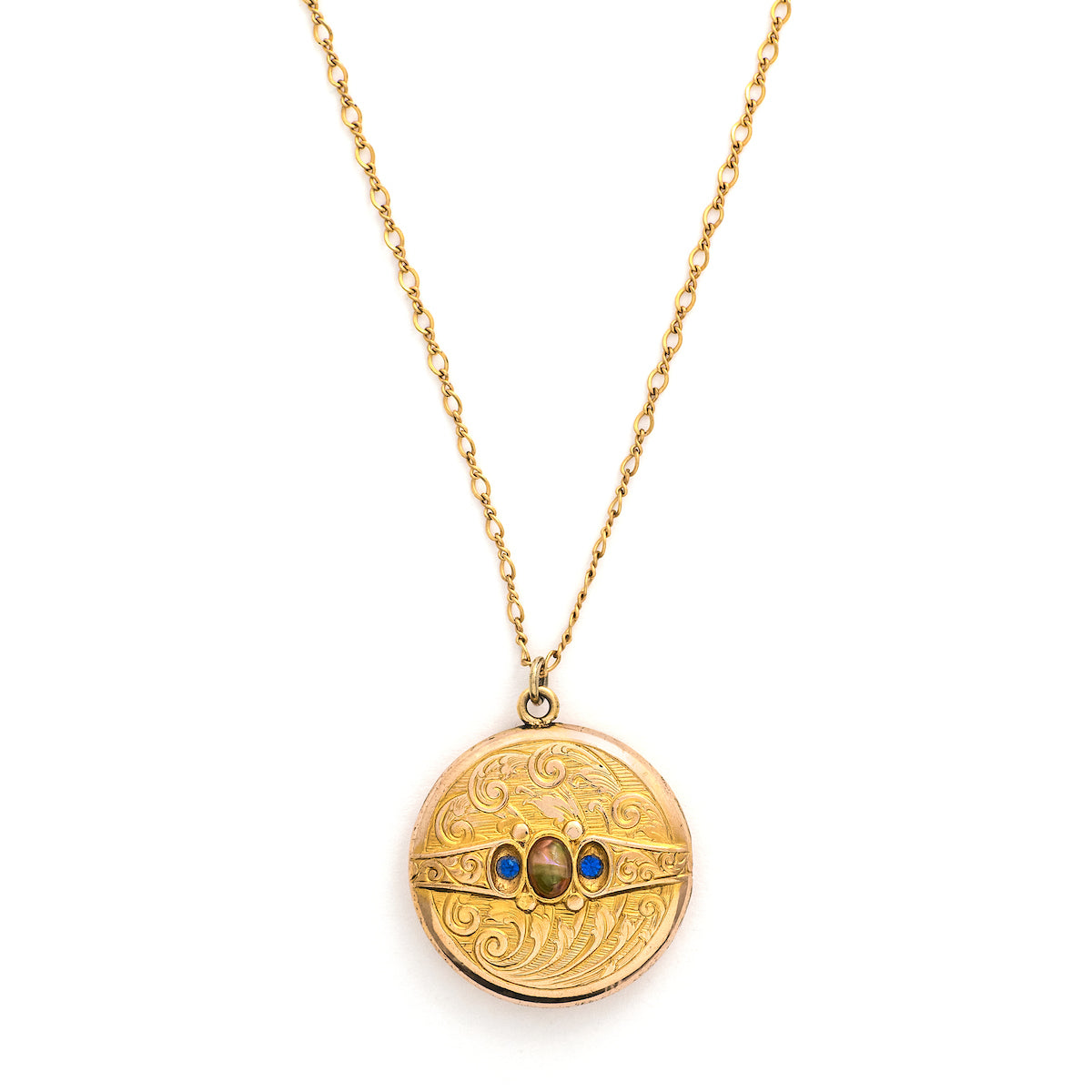 This detailed round locket features an intricate pattern reminiscent of rolling waves with two blue and one multicolored glass stones at it's center. It opens to hold two photos and pairs perfectly with one of our antique gold fill chains.  Front locket view