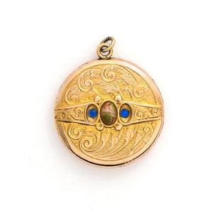 This detailed round locket features an intricate pattern reminiscent of rolling waves with two blue and one multicolored glass stones at it's center. It opens to hold two photos and pairs perfectly with one of our antique gold fill chains.  Front locket view