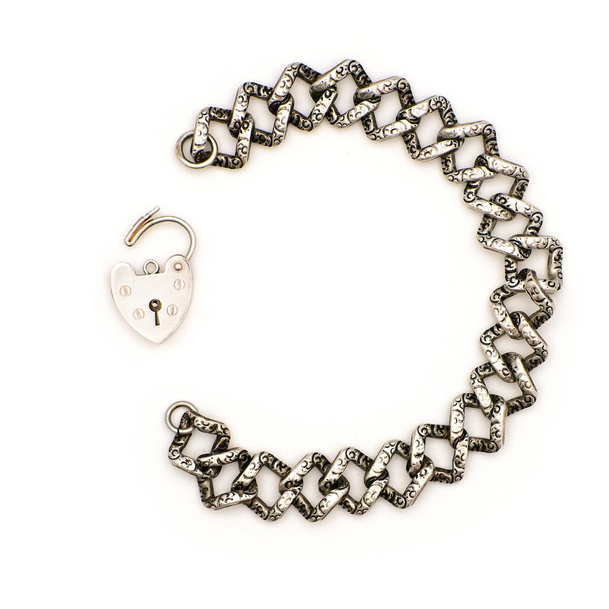 This Vintage Silver Lock Bracelet features a heart shaped lock that is able to open, on a 7" curb chain. On one side of the chain are hand engraved markings, giving the bracelet an edgy feel. Worn simply on its own or made into a statement piece by adding charms, this bracelet has many possibilities. Front bracelet view